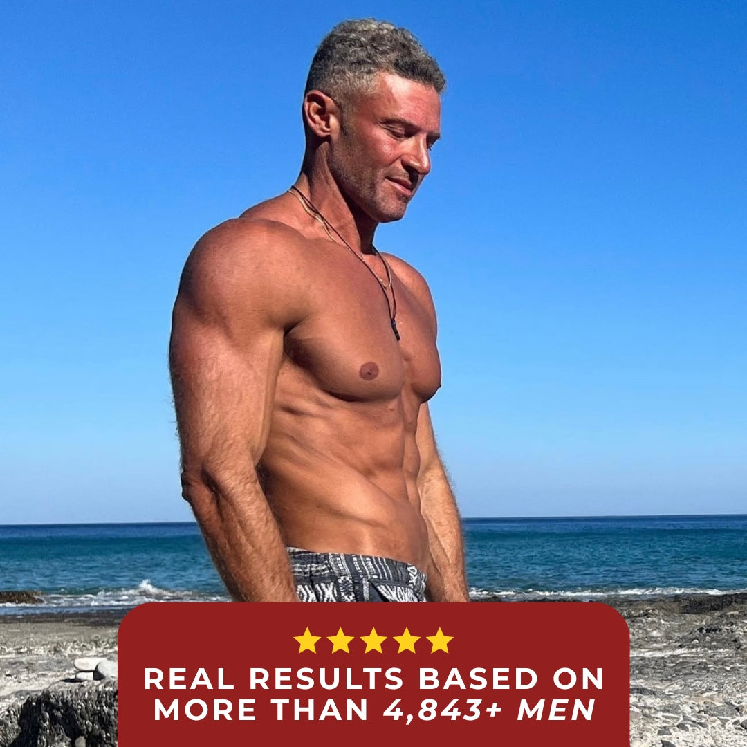A muscular man standing on a beach, smiling with the ocean in the background.