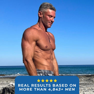 A man with a toned physique standing on a beach, smiling while looking down sharing a testimonial.